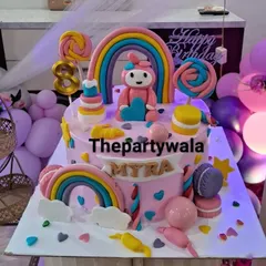 A colorful rainbow-themed cake with lollipops and macarons, perfect for a sweet celebration.