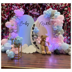 A chic and modern baby shower backdrop celebrating 'Baby Mehta on the way'. The design uses a soft blue and pink palette with a crescent moon detail, balloon garlands, and a large teddy bear for a dreamy welcome.