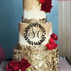 Love is in the details. This golden and red wedding cake radiates warmth and regal charm, featuring a dramatic gold-leafed bottom tier and crowned with rich red sugar roses.