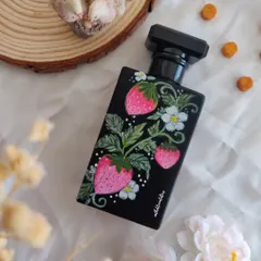 A hand painted perfume bottle featuring sweet, juicy strawberries. The vibrant pink and red of the berries pop against the black glass, creating a whimsical and fresh design that's full of character.