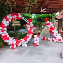 A heart-themed balloon decoration for an outdoor event. This large, heart-shaped arch is made of red, pink, and white balloons, creating a romantic and festive atmosphere.
