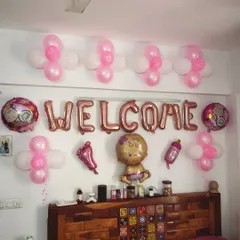 A simple and sweet 'Welcome' decoration for a baby girl. The setup uses pink and white balloons and various baby-themed foil balloons over a headboard.