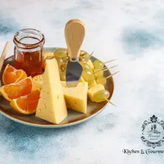 A simple yet elegant cheese plate featuring wedges of hard cheese, fresh grapes, and orange slices, served with a small jar of honey. This highlights the classic and timeless pairing of cheese and fruit.
