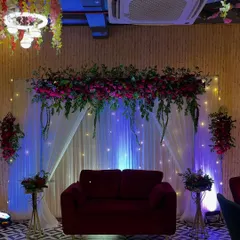 This is an elegant stage setup I created for a Roka ceremony in a restaurant. The combination of a rich red velvet sofa, a lush floral arrangement overhead, and soft fairy lights against a white curtain backdrop creates a sophisticated and romantic ambiance.