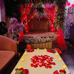 This image focuses on the small details that make the setup special. A table is decorated with scattered red rose petals and surrounded by warm, flickering battery-operated candles for a safe and romantic ambiance.