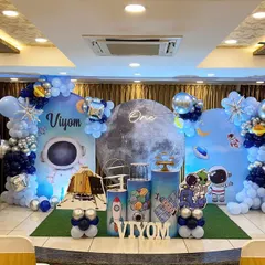 An out-of-this-world space theme for a first birthday party. This full setup includes a custom moon and planet backdrop, astronaut and rocket ship props, and a galaxy-inspired balloon arrangement to create an unforgettable adventure.
