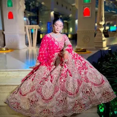 A full-length shot of a bride in her magnificent red lehenga, her hair styled in a secure floral bun. This showcases how a classic updo complements a grand bridal outfit perfectly.