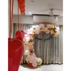 A sophisticated decoration for a couple's birthday party at home, with a pastel and gold balloon arch and hanging heart balloons.