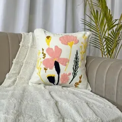A beautiful floral embroidered boho cushion cover, styled on a sofa. The mix of pink and yellow flowers on a neutral base adds a soft, feminine touch.