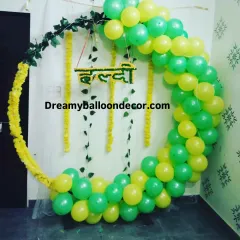 A simple yet elegant Haldi backdrop. This design combines a balloon ring in yellow and green with marigold flower garlands for a fresh, traditional feel.