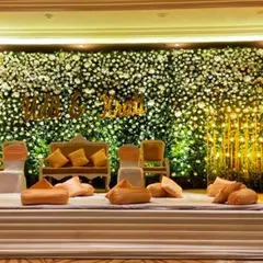A stunning reception stage featuring a full wall of white and green flowers. The couple's names in gold lettering and the warm floor lighting create a dreamy and romantic ambiance.
