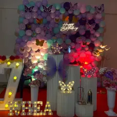 A butterfly garden theme against a full balloon wall. This immersive decoration uses pastel balloons, various butterfly cutouts, a 'Happy Birthday' neon sign, and light-up letters and numbers.
