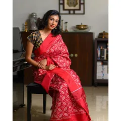 A woman seated gracefully in a stunning red saree. This indoor portrait uses the environment, including the piano, to add a touch of sophistication.