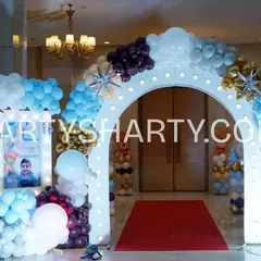 A grand entrance for a teddy bear themed party. The illuminated arch is decorated with blue, white, and gold balloons, with a personalized welcome sign featuring a photo of the birthday boy. A red carpet adds a touch of VIP treatment.