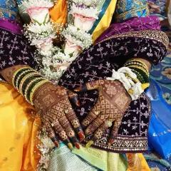 A beautiful shot of a Marathi bride's hands, showcasing the rich, dark stain of her bridal mehendi. The color contrasts beautifully with her traditional green bangles and wedding attire.