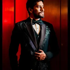 A dapper groom portrait from the Sangeet night. The dramatic red lighting and his sharp tuxedo create a look of pure sophistication and style.