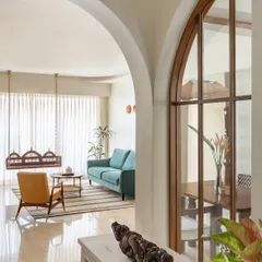 Arches are a recurring motif we use to soften spaces and add a traditional touch. Here, an archway frames a view of the living room, where a classic wooden swing and a comfortable teal sofa create an inviting atmosphere for relaxation.