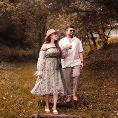 A candid moment of the couple, showing how their outfits work together in the woodland setting. His simple white shirt and trousers complement her floral dress, creating a cohesive and relaxed look.