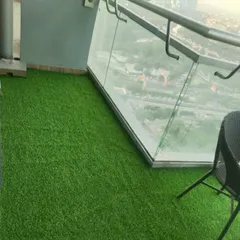The glass railing on this high-rise balcony reflects the green of the new artificial grass floor.