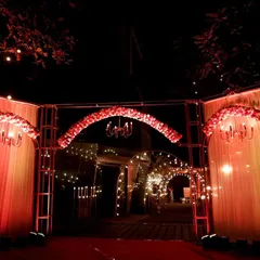 A grand entrance designed for a Sangeet night in Lonavala. The structure features red floral arches, classic chandeliers, and warm string lights, setting a dramatic and celebratory tone for an evening of 'Nacho Tappo'.