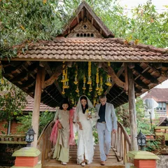 A bride is escorted over a charming wooden bridge at a resort in Kerala, showcasing a beautiful destination wedding with cross-cultural elements.