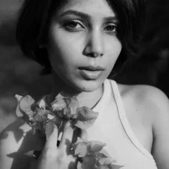 A close-up black and white portrait where the model is holding flowers. The soft natural light and monochrome treatment create a timeless and gentle mood.