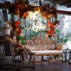 This "Better Together" setup combines industrial and boho elements. A black metal frame is softened with a rattan bench and lush, autumn-toned floral arrangements, creating a modern yet romantic photo spot.