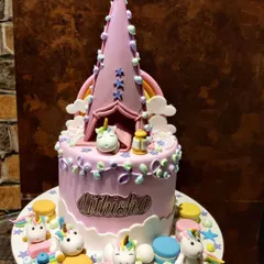 A closer look at my unicorn campsite cake. The design features a tall, pointed tent topper and several small, detailed unicorn figures enjoying a party at the base of the cake.