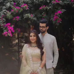 A classic portrait of a couple at their Mehendi ceremony, framed by beautiful pink bougainvillea. Their elegant, coordinated outfits and the lush floral background create a timeless and romantic image.