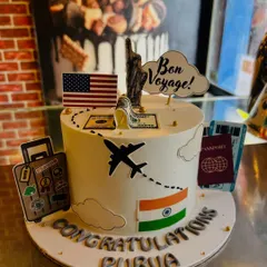 A "Bon Voyage" cake for Purva, celebrating her journey to the USA. The cake is decorated with flags, a passport, and the Statue of Liberty.