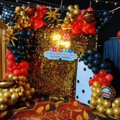 A vibrant photo booth for a Diwali card party. The decor features a gold sequin wall, a 'Let's Party' neon sign, and a balloon arch in red, black, and gold chrome balloons.