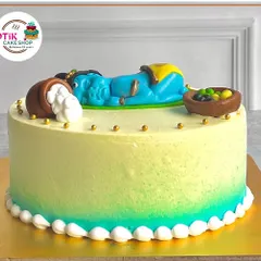 A beautiful Janmashtami cake featuring a fondant figurine of baby Krishna sleeping next to a pot of spilled butter. The green and yellow ombre effect adds a divine touch.