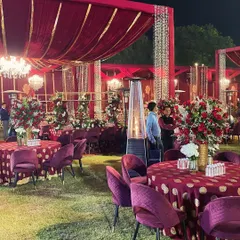 A glimpse of a royal-themed wedding reception on a lush lawn. The decor features rich maroon tablecloths with gold polka dots and plush velvet chairs, combining traditional colors with luxurious textures for an opulent feel.