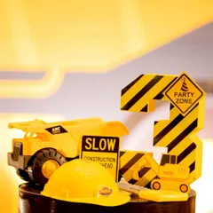 A close-up of a tabletop decoration for a third birthday. It features a toy dump truck, a mini hard hat, and a custom-made number '3' with construction stripes, showing my attention to even the smallest details.