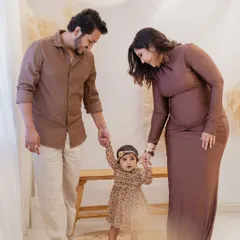 A precious moment of a baby's first steps. The proud parents hold their daughter's hands, guiding her as she walks on a small rug in the studio during her first birthday family session.