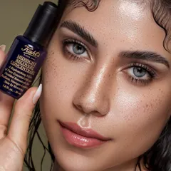 Here, the focus is on real, beautiful skin, complete with natural freckles. The model holds the Kiehl's Midnight Recovery Concentrate, creating a direct link between the product and the resulting dewy complexion. The wet-look hair adds to the overall feeling of hydration and freshness.