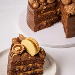 A slice of luxury. This cake features a moist dark chocolate sponge, 54% Belgian dark chocolate ganache, and a crunchy blend of hazelnut praline feuilletine, topped with Ferreros and macarons.