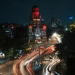 A long-exposure shot of Mumbai's Municipal Corporation Building at night, with light trails from traffic creating rivers of light. This image shows the city's constant motion, a blend of historic architecture and relentless modern energy.