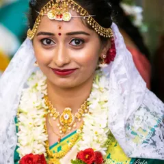 A close-up of a smiling bride on her wedding day. This highlights the traditional bindi, gold jewelry, and the delicate white veil used in many South Indian ceremonies.