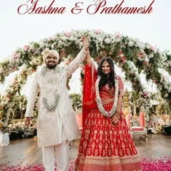 The "just married" feeling! The couple raises their hands in victory after the varmala, under a beautiful floral arch, with petals raining down on them. A picture of pure happiness.