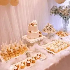 Another angle of the cloud-themed dessert table, showing the two-tiered cake and an array of carefully arranged cupcakes, cake pops, and pastries. The delicate baby's breath in the background adds to the light and airy feel.