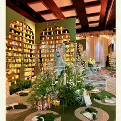 A tablescape from a greenhouse-themed engagement. The deep green tablecloth is a rich base for the wild, unstructured floral centerpiece, while the wall of candles in the background casts a warm, romantic glow over the entire setting.