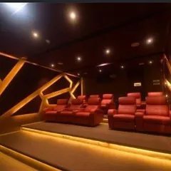 This modern theater features tiered red leather recliners and unique geometric wall panels with backlighting. The combination of ambient and accent lighting creates a sophisticated and dynamic space for watching movies.