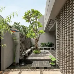 A minimalist Zen garden in a courtyard, featuring a single Plumeria tree, a small water channel, and textured brick walls. This design creates a peaceful and contemplative space.
