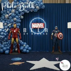 A dedicated photo booth for the Marvel theme, featuring life-size statues of Iron Man and Captain America. The neon Marvel logo and blue drapery provide a clean, powerful backdrop for superhero poses.