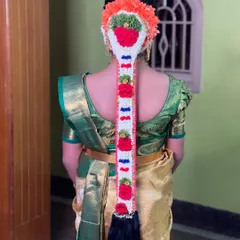 A traditional 'mogginajade' hairstyle for a half-saree ceremony. This style is rich in cultural significance and is decorated with fresh flowers and colorful elements.