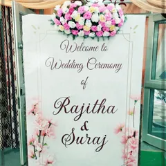 A close-up of a custom wedding welcome sign, featuring elegant calligraphy and a floral motif. Topped with a fresh arrangement of pink and white roses, this sign adds a personal and sophisticated touch to the event entrance.