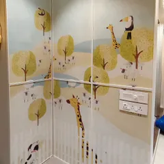A cute and whimsical animal wallpaper installed in a corner. The design with giraffes, sheep, and a toucan is perfect for a nursery or a young child's room.