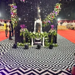 A chic outdoor stage setup with a black shimmer backdrop, elegant floral arrangements, and a unique geometric patterned floor.