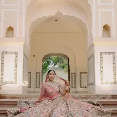 A regal bridal portrait showcasing the bride in her magnificent lehenga. Posed on the steps of a heritage property, this image highlights the intricate details of her attire and the elegance of the setting.